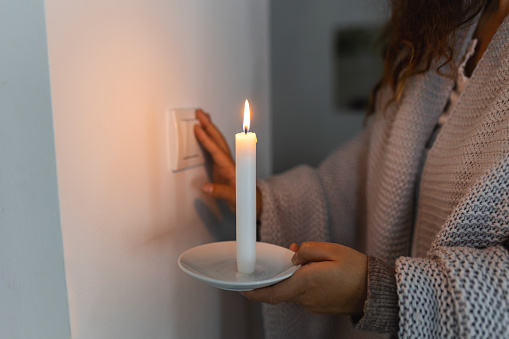 Energy crisis. Hand in complete darkness holding a candle trying to turn on light during a power outage. Blackout concept.
