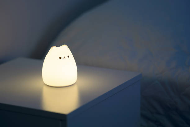 Cute cat shaped night lamp standing on a bedside table next to bed.