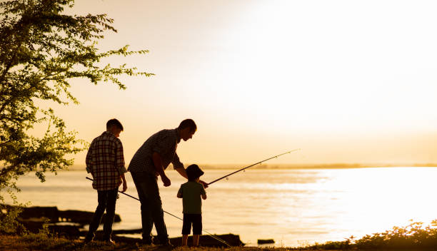 papà di famiglia e due figli stanno pescando al tramonto, sagoma di un uomo e due ragazzi. - fathers day foto e immagini stock