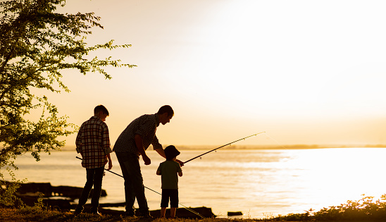 Family dad and two sons are fishing at sunset, silhouette of a man and two boys. Copy space