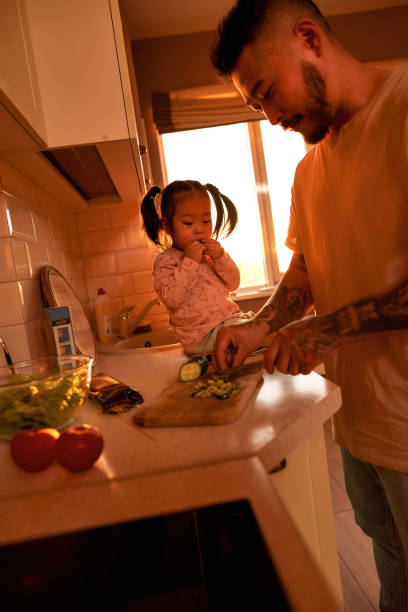 dziewczyna je kawałek ogórka i spójrz na sałatkę taty gotować - sparse healthy eating single father contemporary zdjęcia i obrazy z banku zdjęć