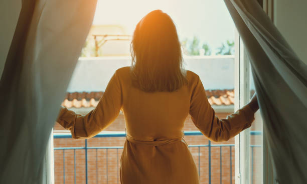 istock Woman enjoys warm summer breeze while standing in front of the window. 1454591375
