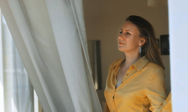 istock Woman enjoys warm summer breeze while standing in front of the window. 1454591382