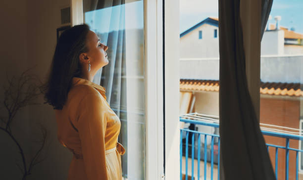istock Woman enjoys warm summer breeze while standing in front of the window. 1454591385