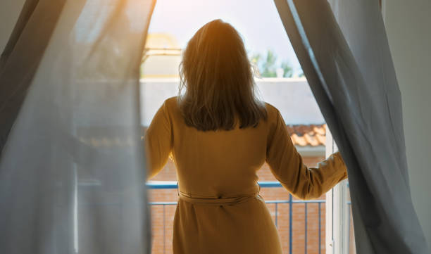 istock Woman enjoys warm summer breeze while standing in front of the window. 1454591436