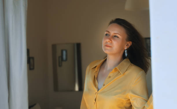 istock Woman enjoys warm summer breeze while standing in front of the window. 1454591441