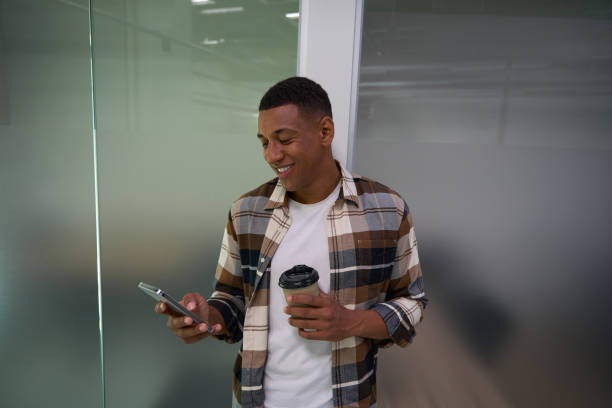 istock Smiling young man typing on phone and holding coffee 1454593320