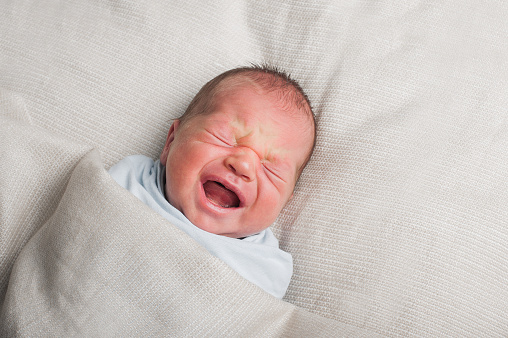 Newborn 3 weeks old screams and cries in dream close-up. Baby care, colic, teething, healthy sleep.