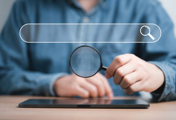 istock Businessman holding magnifier glass on tablet with search icon for Search Engine Optimisation or SEO concept to find information by internet connection. 1454596166