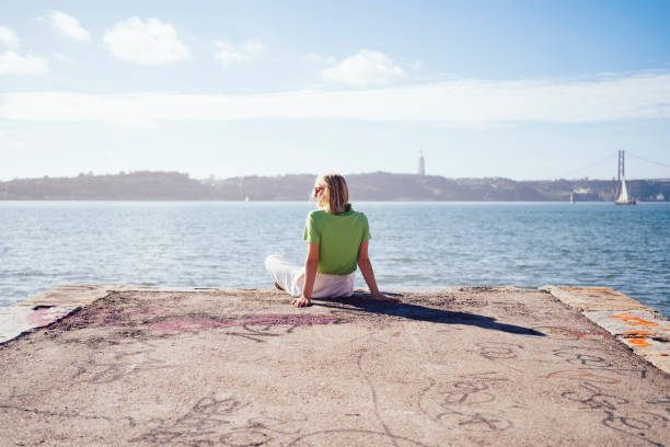Photo of a young woman sitting on the dock; enjoying the view and the calmness of the sea while spending time outdoors, on a warm autumn day.