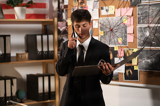 Concentrated detective reading dossier in dark office, calling on phone and speaking