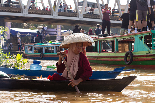 Banjarmasin, Kalimantan - Indonesia – 30 October 2022: everyday in the morning, women in floating market lok baintan, Banjarmasin city, Indonesia paddled their boat to carry out buying and selling various basic needs such as vegetables and crops from villages along martapura river.