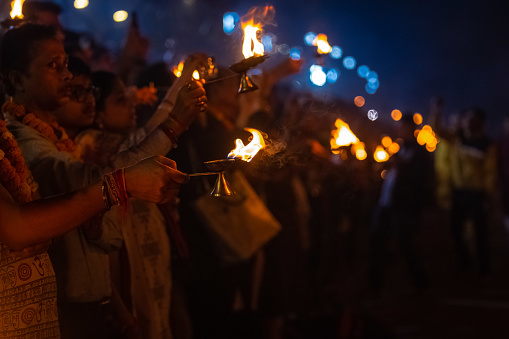 Rishikesh, Uttarakhand, India - October 2022: Portrait of hindu devotees performing river Gange aarti with fire flame in hand at triveni ghat to worship river ganges. Ganga aarti performed in night.