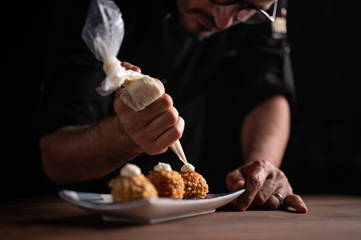 A male chef squeezing cream on meatballs.