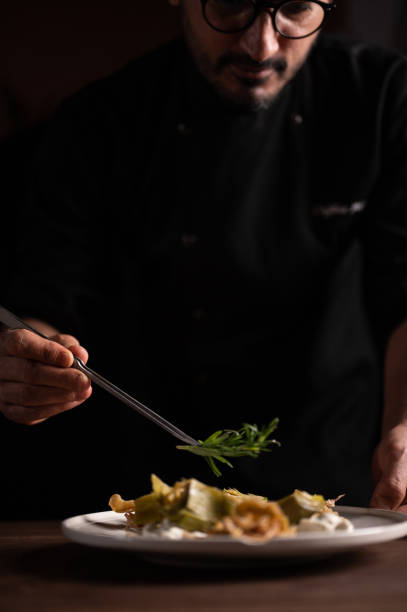 A male chef decorating a plate of artichoke stock photo