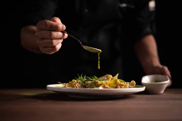 A male chef pouring sauce on on a plate of artichoke stock photo