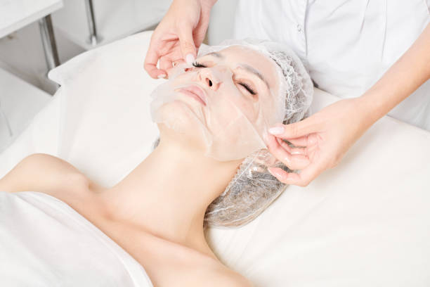 esteticista alisa la mascarilla de la hoja en la cara de la mujer para rehidratar la piel de la cara, procedimiento en el salón de belleza - rehydrate fotografías e imágenes de stock