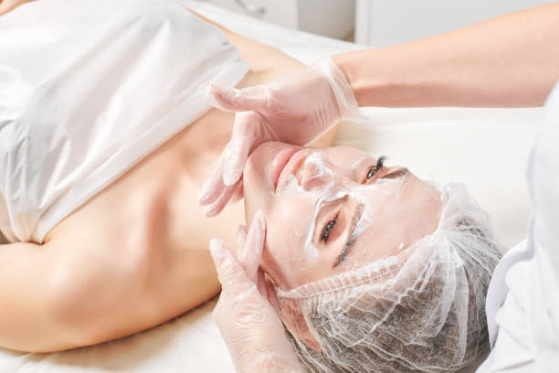 Cosmetologist massages cream mask into woman face skin for rejuvenation, procedure in beauty salon stock photo