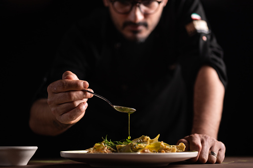 A male chef pouring sauce on on a plate of artichoke.