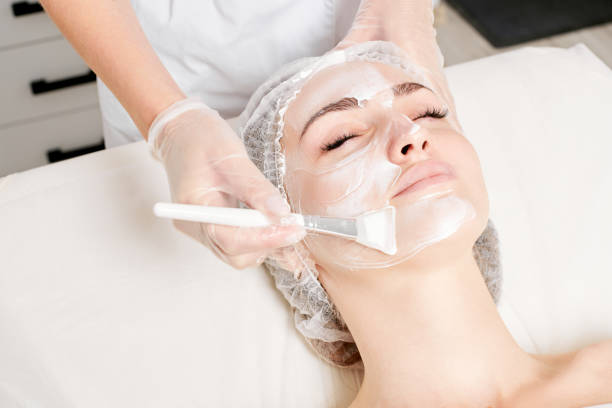 Beautician applies vitamins cream mask on woman face for rehydrate face skin in beauty salon stock photo