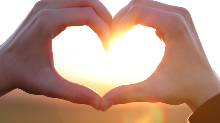 Hands in shape of love heart at sunset