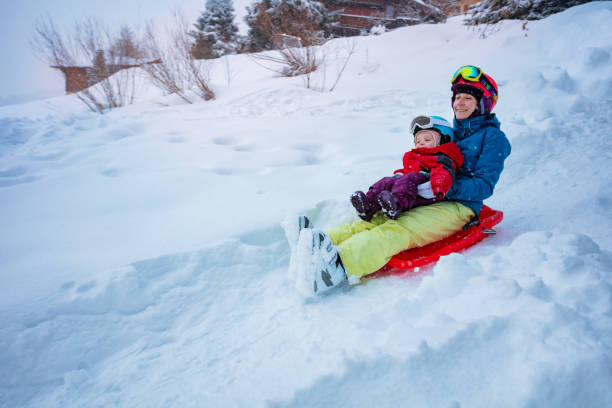 mutter mit kleinem mädchen schlittert bergab auf dem schlitten vom hügel - little boys sled clothing slide stock-fotos und bilder