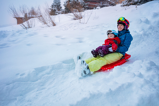 Mother with little girl sled downhill on the sledge from the hill at winter vacations