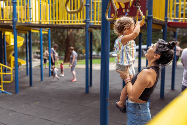 Nanny helping little girl use playground jungle gym A young Latin American woman helps a two year old girl use the jungle gym at the playground on a warm sunny afternoon. asian nanny stock pictures, royalty-free photos & images