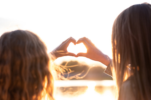 two little girls show heart at sunset