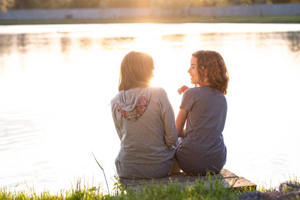 istock Rear view two girls sitting at riverbank 1454632068