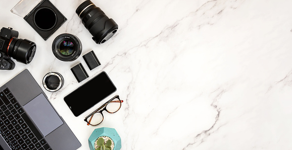 Modern layout of white marble desk of photography with laptop, camera, eyeglasses, smart phone and lenses. Copy space on right side for advertisement