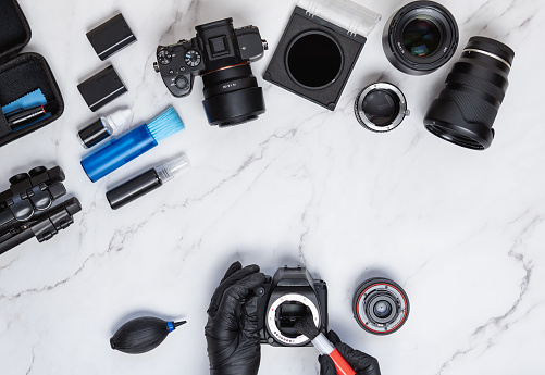 Modern camera cleaning kit layout on white marble background with hand wearing gloves while cleaning sensor. Photography and entrepreneur concept