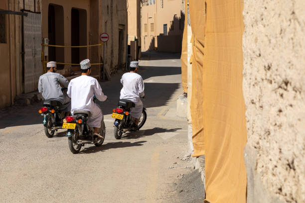 Three people on motorcycles travel through the narrow streets of the city of Nizwa. Traditional medieval architecture in Nizwa, Oman. stock photo