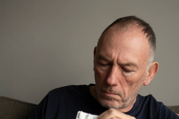 Senior man suffering with cold and flu symptoms. He is taking cold remedy capsules.