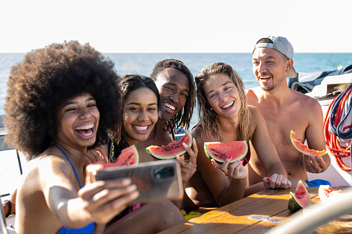 Happy multiracial friends making selfie while eating watermelon at boat party, young people having fun in sea tour, travel and luxury vacation concept, selective focus