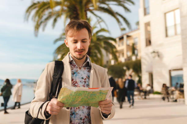 istock Handsome young tourist holding a map while wearing a backpack in a city 1454660060