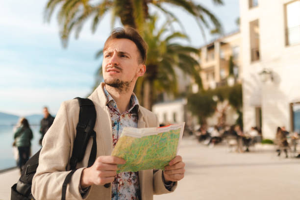 istock Handsome young tourist holding a map while wearing a backpack in a city 1454660064