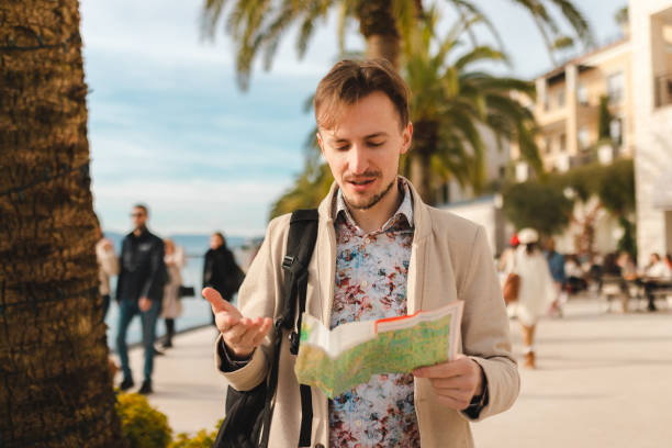 istock Handsome young tourist holding a map while wearing a backpack in a city 1454660084
