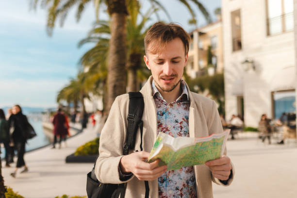 istock Handsome young tourist holding a map while wearing a backpack in a city 1454660085