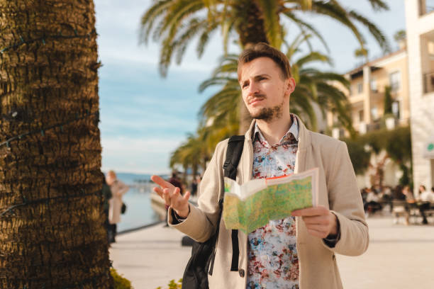 istock Handsome young tourist holding a map while wearing a backpack in a city 1454660091