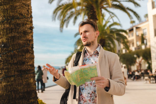 istock Handsome young tourist holding a map while wearing a backpack in a city 1454660092
