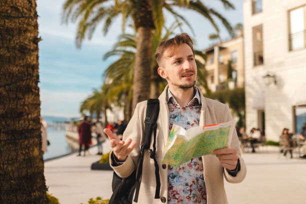istock Handsome young tourist holding a map while wearing a backpack in a city 1454660095