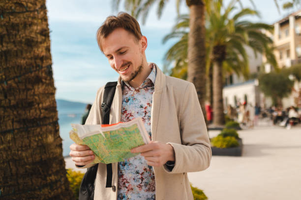 Smiling young man holding a map while on a vacation by the sea