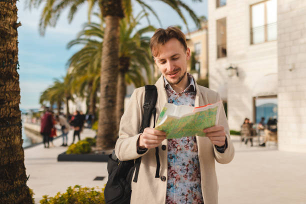 istock Smiling young man holding a map while on a vacation by the sea 1454660098