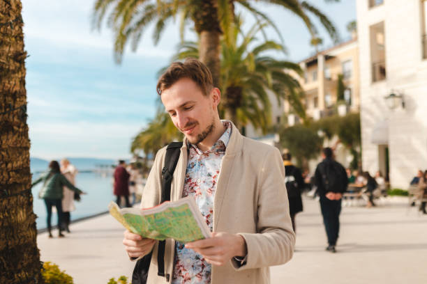 istock Smiling young man holding a map while on a vacation by the sea 1454660112