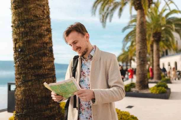 istock Smiling young man holding a map while on a vacation by the sea 1454660113