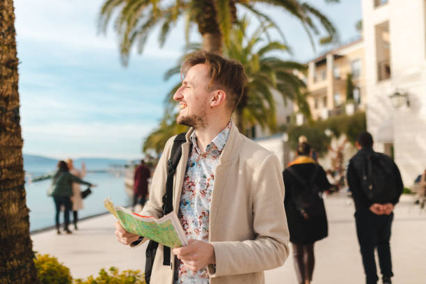 istock Smiling young man holding a map while on a vacation by the sea 1454660115