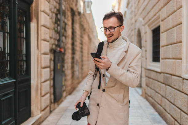 istock Handsome young man using his phone while on vacation visiting an old town 1454661352