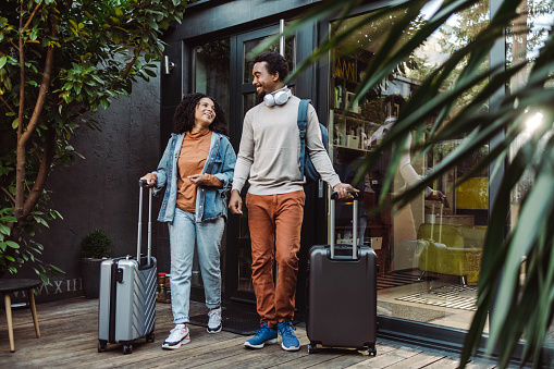 Happy young couple of African-American tourists with suitcases