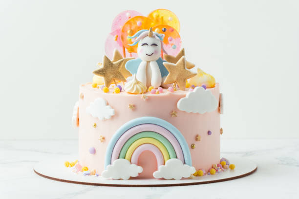 unicorn cake with pink cream cheese frosting decorated with mastic rainbow, multicolored caramel candies and unicorn shaped figure on top. birthday cake for a little girl on the white background - little cakes imagens e fotografias de stock